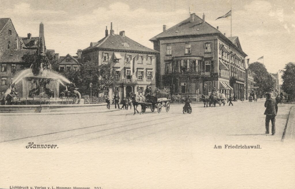 Historische Postkarte: der Friedrichswall um 1900 mit Brunnen und dem Wangenheimpalais, dem damaligen Rathaus, davor Passanten und Fuhrwerke